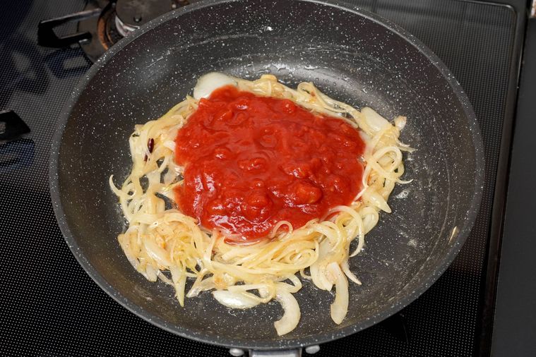 炒めた玉ねぎとトマト缶がフライパンに入っている様子