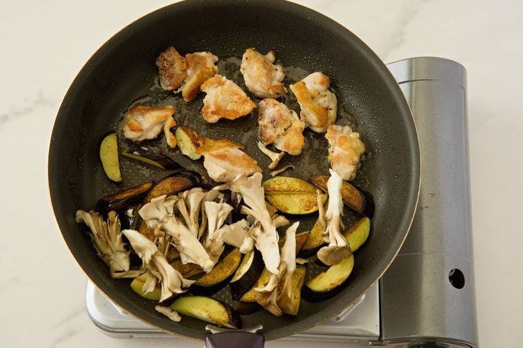 フライパンに入った鶏もも肉となすとまいたけ