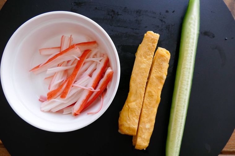 下ごしらえ済みのカニ風味かまぼこ、厚焼き卵、きゅうりが並ぶまな板