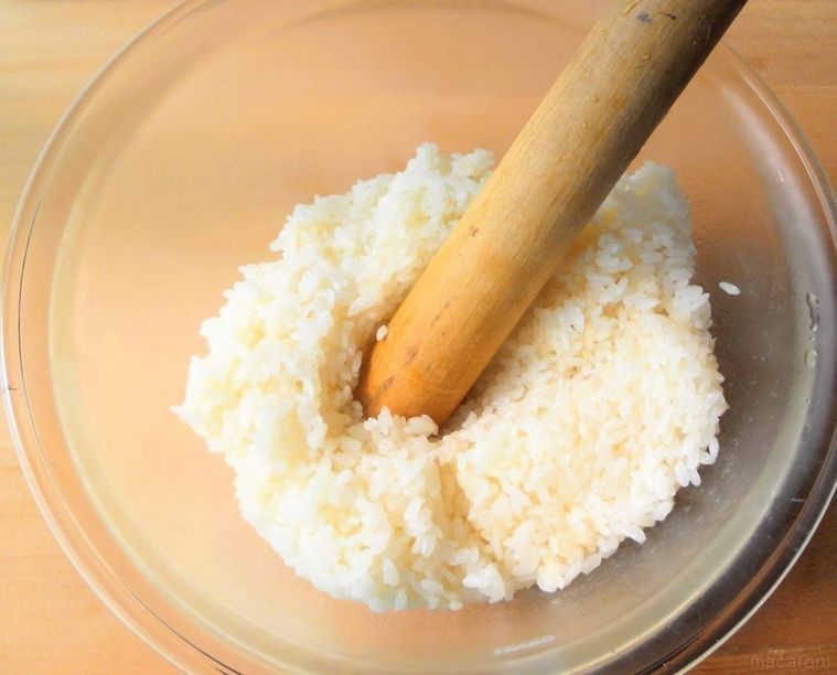 炊いたもち米と米を透明なボウルに入れて、すりこぎでつぶしている様子