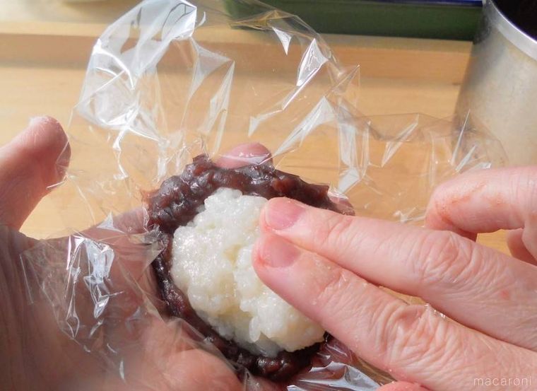 手の上でラップの上につぶあんを広げ、もちだねをのせている様子