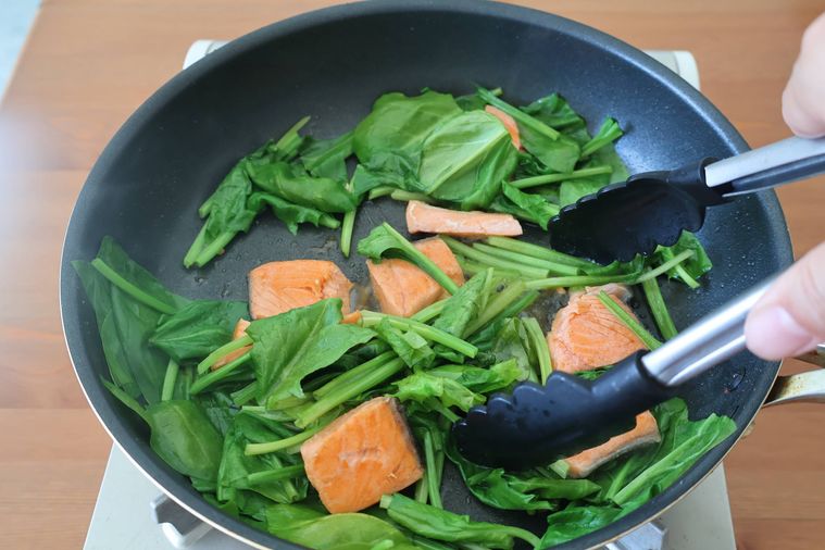 フライパンでほうれん草を鮭を炒めている
