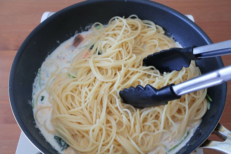 フライパンでソースとパスタを和えている