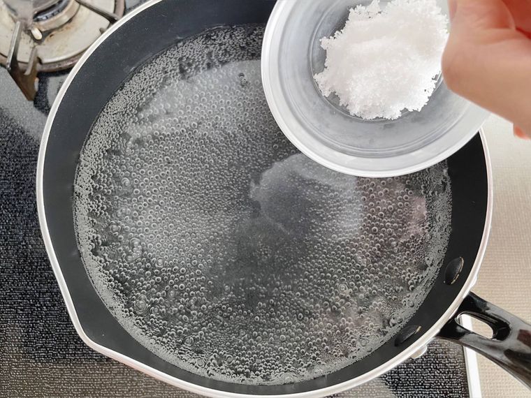 鍋で沸かしたお湯に塩を入れる様子
