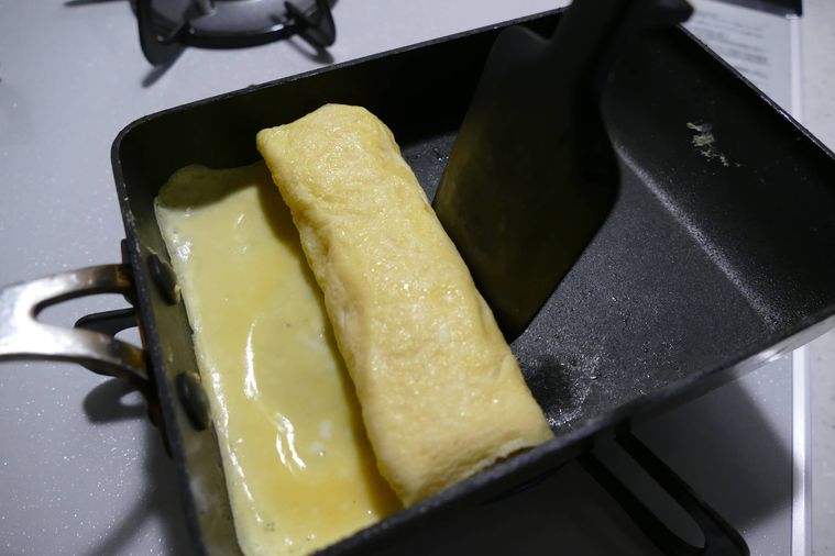 卵焼きを置くから手間に折りたたみながら巻く様子