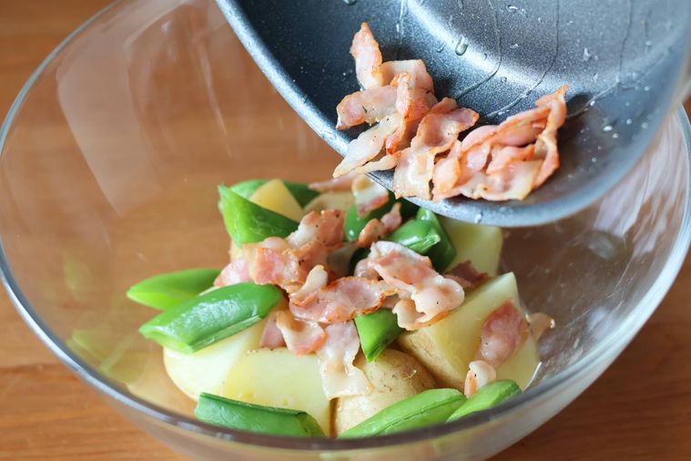 野菜の入ったボウルにベーコンを加えている