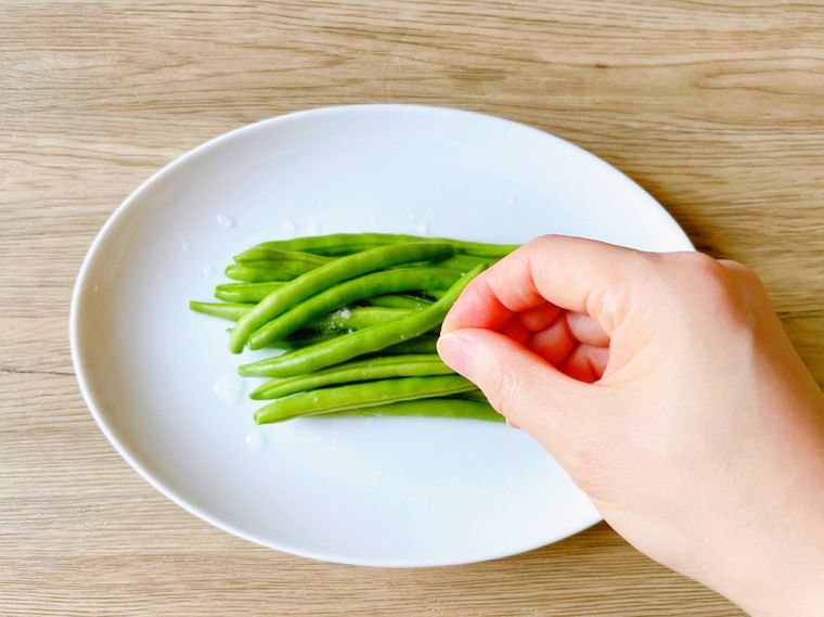 白い皿に盛ったいんげんに塩を振る様子
