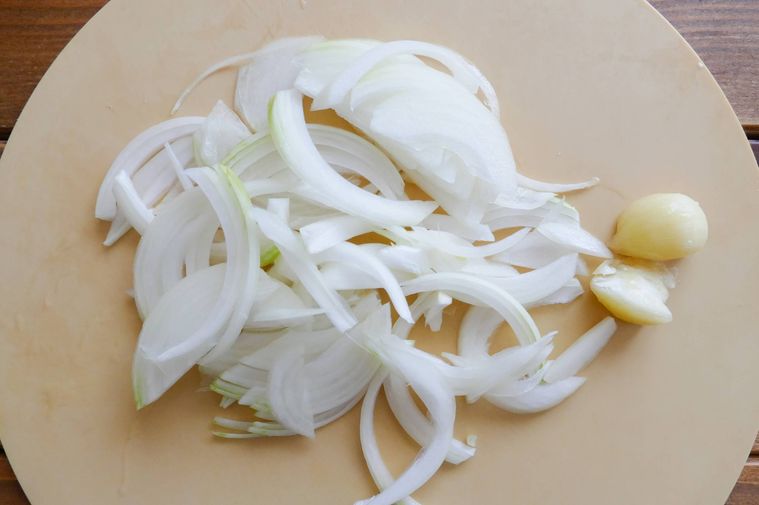 薄切りの玉ねぎと潰したにんにくがのっているまな板