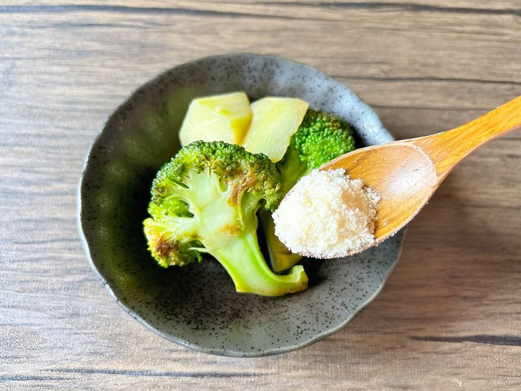小皿に取り分けた炒めブロッコリーに粉チーズをふる様子