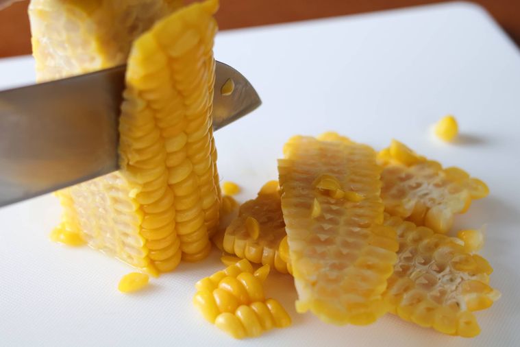 とうもろこしの実を包丁で削いでいる