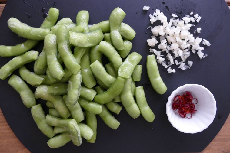 さやの両端を切り落とした枝豆、みじん切りのにんにく、輪切り唐辛子が並ぶまな板