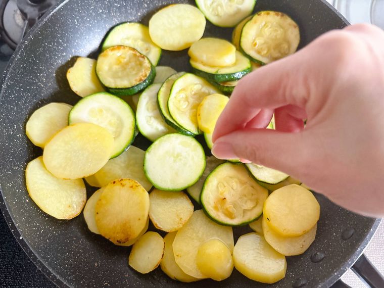 焼き色が付いたズッキーニとじゃがいもに塩をふる様子