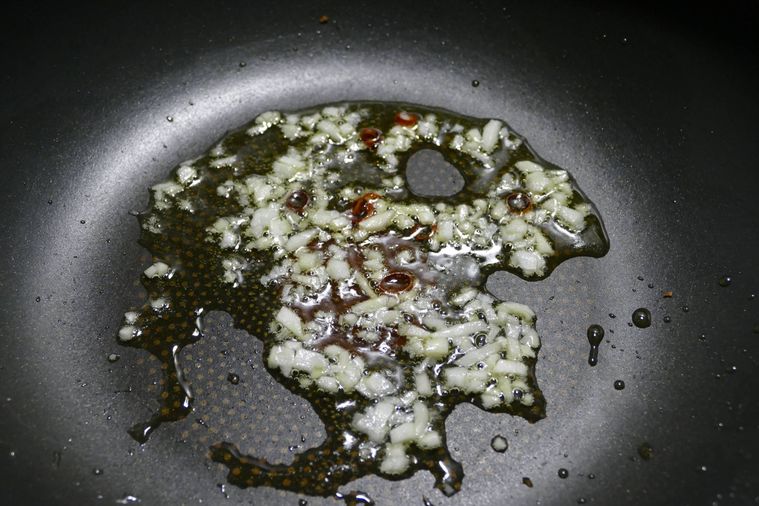 オリーブオイルでにんにくと輪切り唐辛子を炒める様子