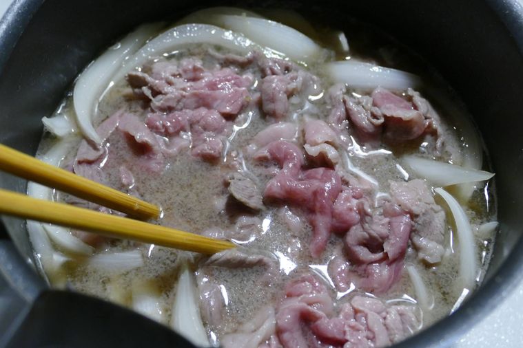 牛こま肉を入れて箸でほぐす様子