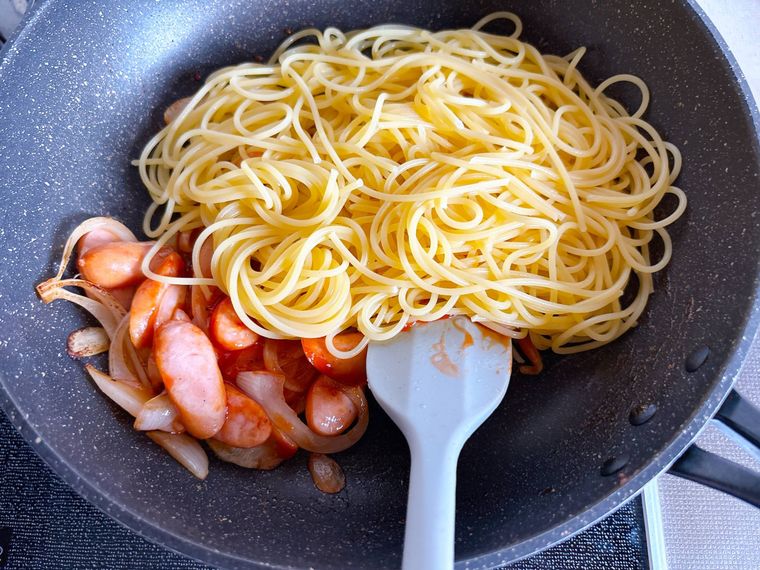 ウインナーソーセージと玉ねぎを炒めたところにスパゲッティを加えた様子