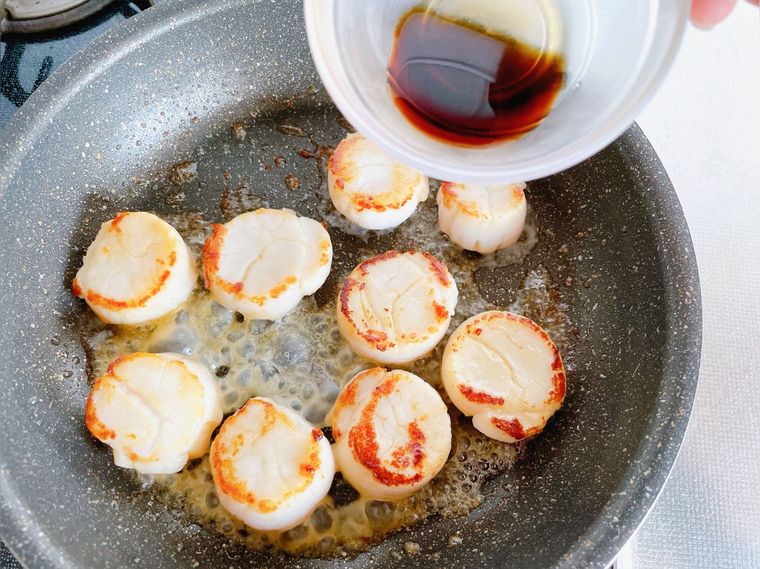 ホタテのバター焼きにしょうゆを回しかける様子