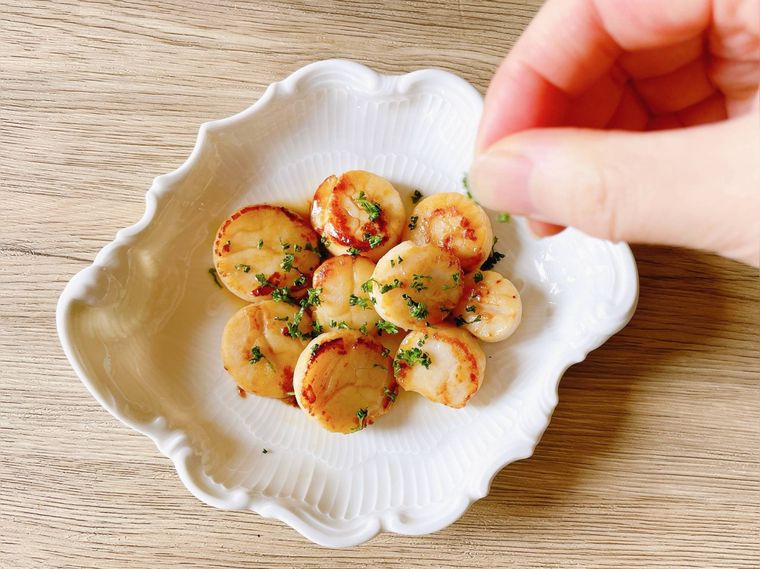 白い皿に盛ったホタテのバター焼きにパセリを振る様子