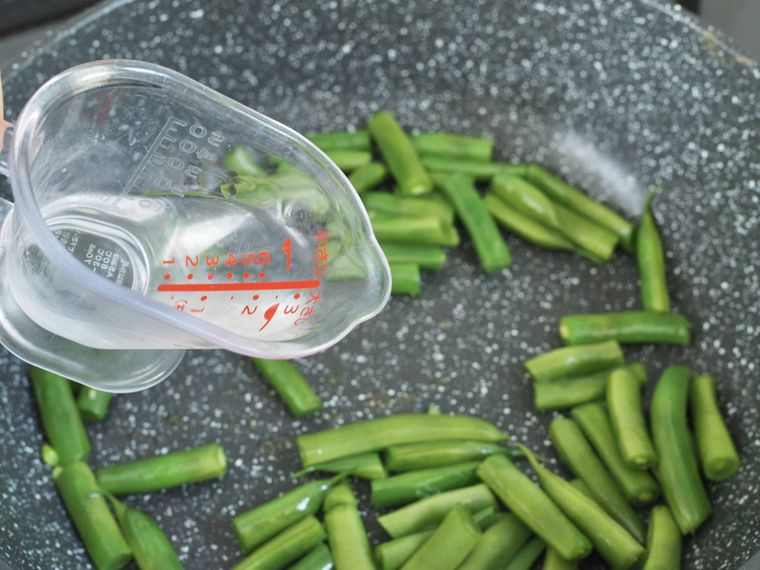 炒めたいんげんに酒をまわし入れている様子