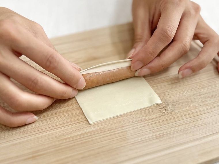 ワンタンの皮でウインナーソーセージを巻いている様子
