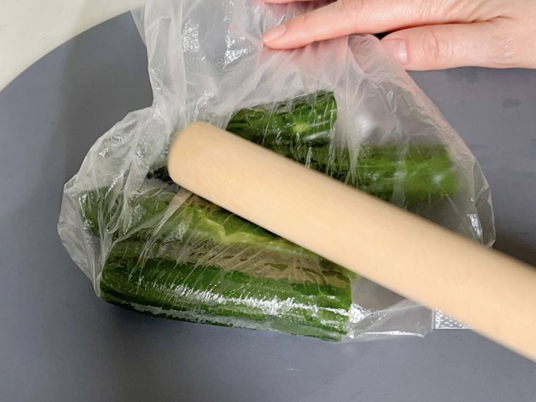 グレーのまな板の上で麺棒で叩かれているポリ袋に入ったきゅうり