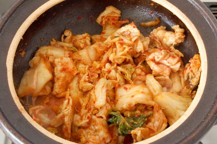 土鍋で豚ロース肉と白菜キムチを炒めている様子