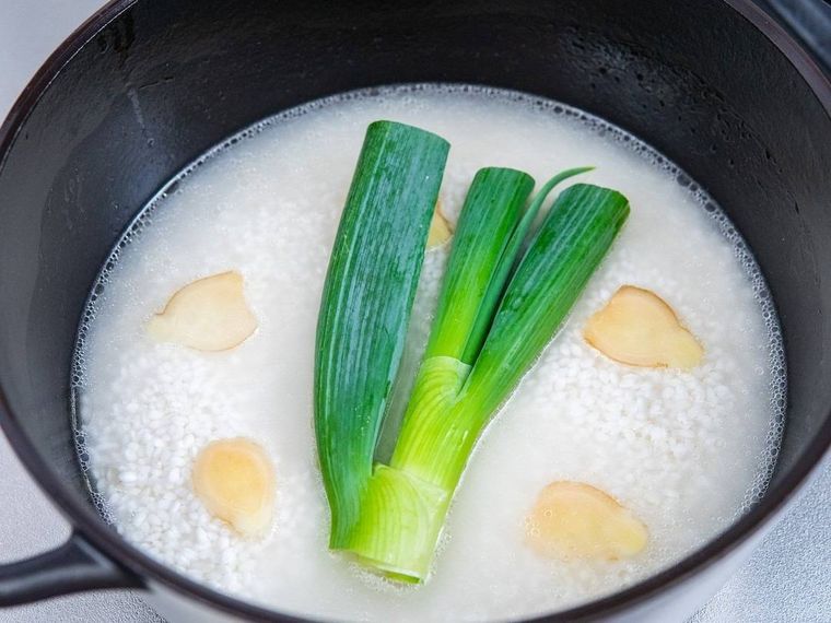 ホーロー鍋に入った米の上に長ねぎ、しょうがの薄切りを置く様子