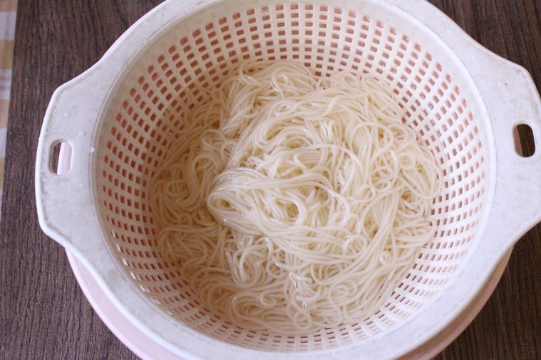 ザルに入ったそうめんをピンク色のボウルに入れ、氷水で締めている様子