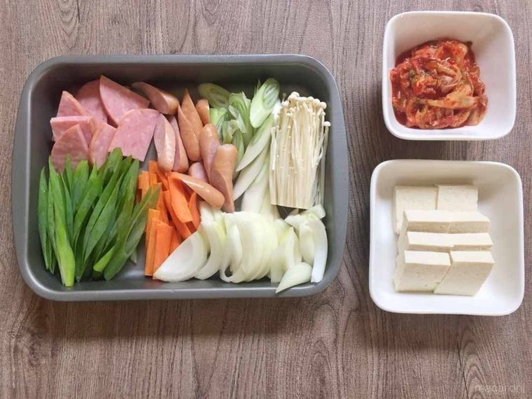 バットや小皿に入ったプデチゲの材料がテーブルに並んでいる様子