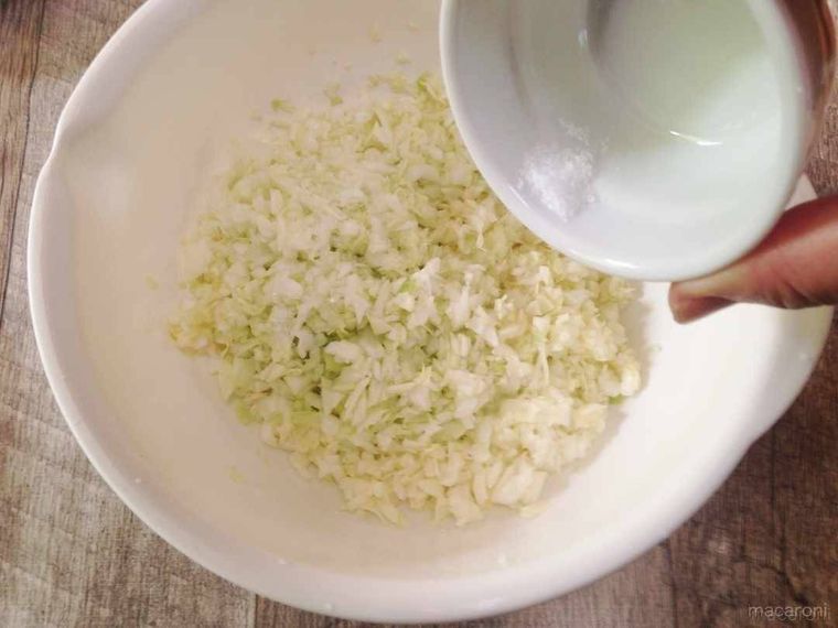 白いボウルに入ったみじん切りキャベツに塩を振り入れる様子