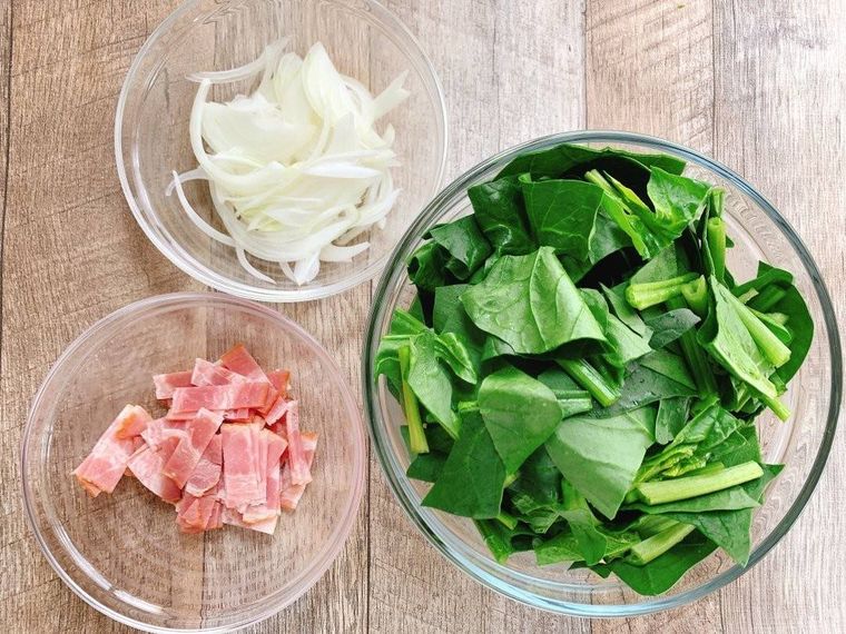 切り分けた玉ねぎ、ベーコン、ほうれん草が入った透明なボウル