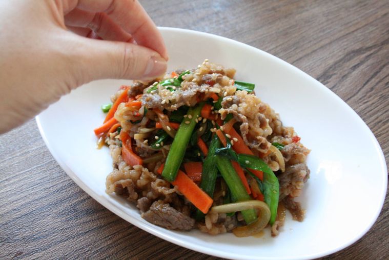 皿に盛りつけたプルコギに白ごまをトッピングしている様子