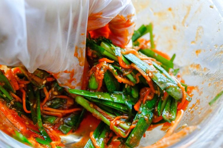 手袋をした手で調味料とニラ、にんじんを混ぜる様子