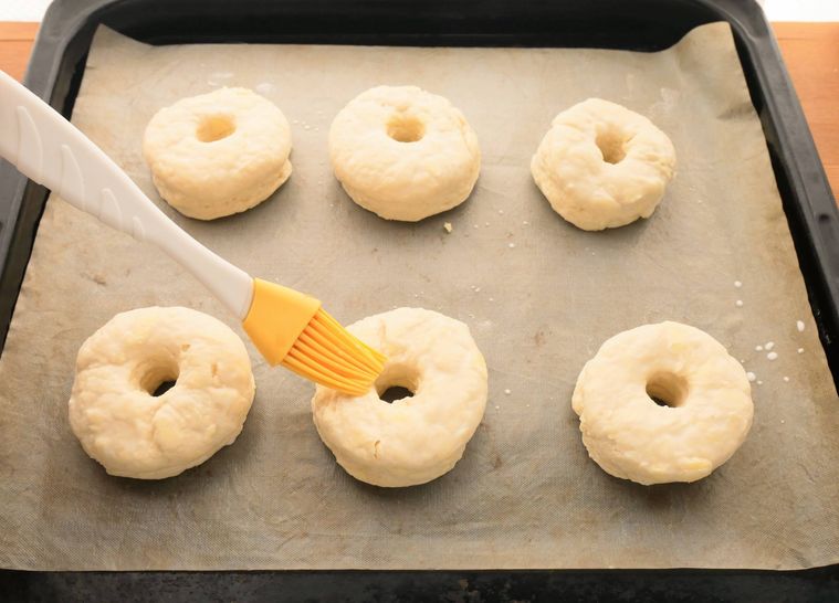 ドーナツ型の生地の表面に、はけで牛乳を塗る様子