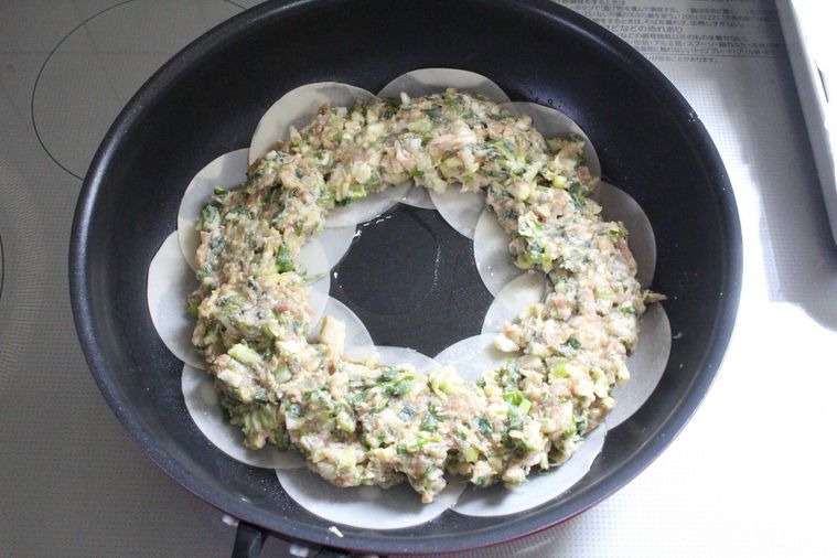 フライパンに餃子の皮、その上にタネがのせられている様子