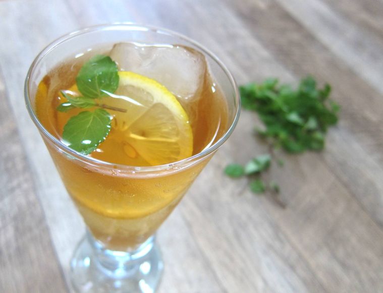 ガラスのグラスに入ったティーソーダにミントの葉とレモンの輪切りを添えている