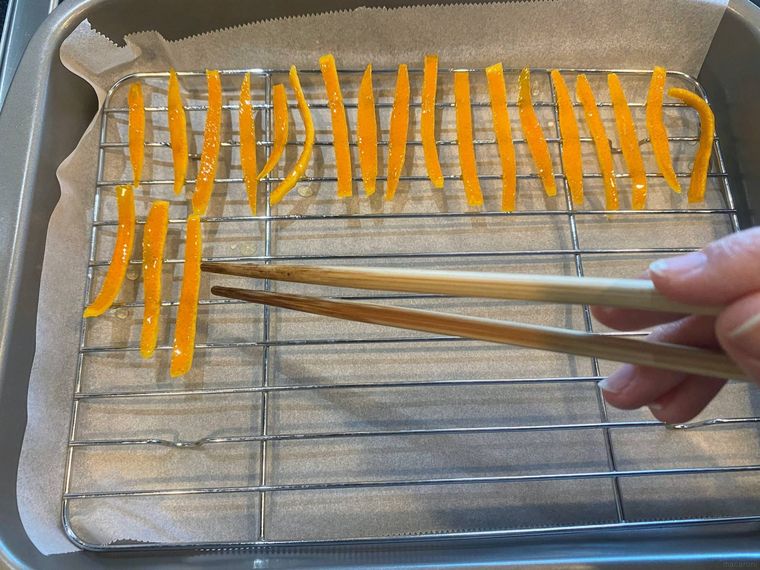 クッキングシートを敷いた網の上にオレンジピールを並べる様子