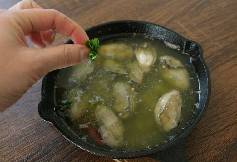 牡蠣のアヒージョにイタリアンパセリをかけている様子