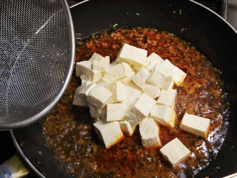 煮立った合わせ調味料に豆腐を加えている様子