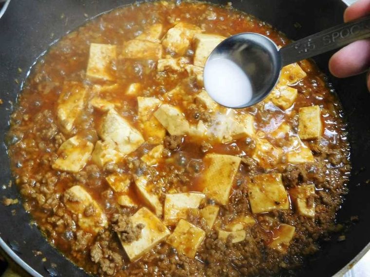 豆腐と合わせ調味料が煮立っているフライパンに水溶き片栗粉を加えている様子