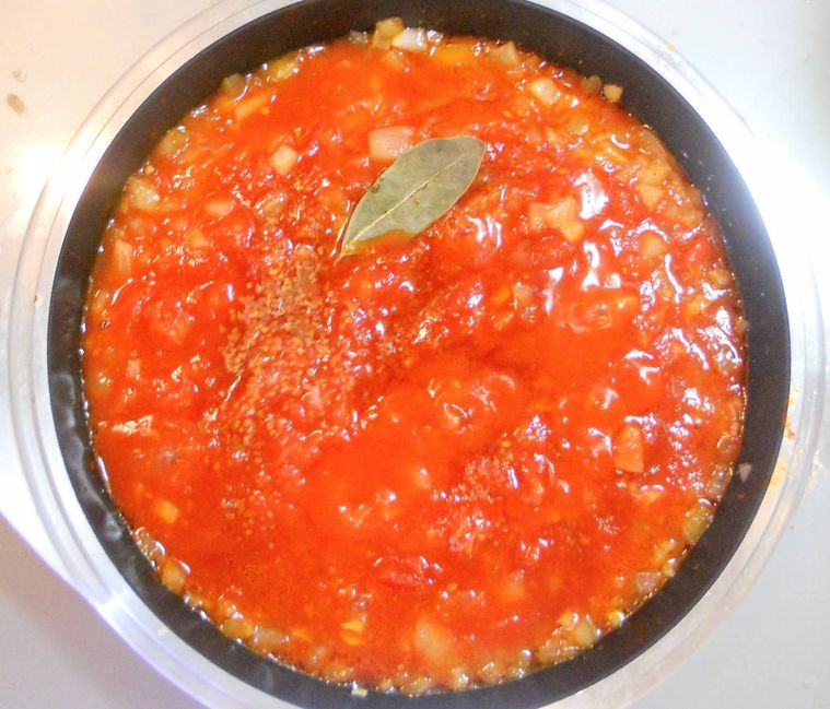 鍋に入ったトマトソースにローリエ、コンソメ、砂糖、水を加え煮ている様子