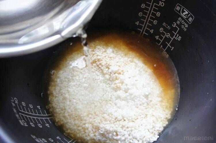 炊飯釜に入った米と調味液に、水を注いでいる様子