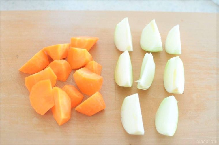 木のまな板に置かれた、乱切りのにんじんとくし切りの玉ねぎ