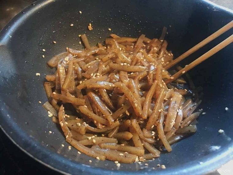 フライパンの中のこんにゃくに白いりごまをふりかけた様子