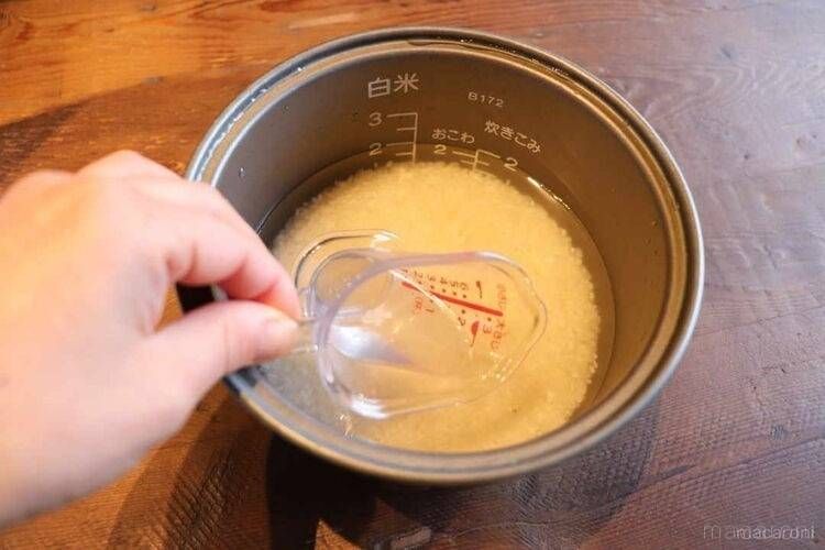 炊飯釜にお米と2合分の水を入れ、カップで水を抜き取る様子