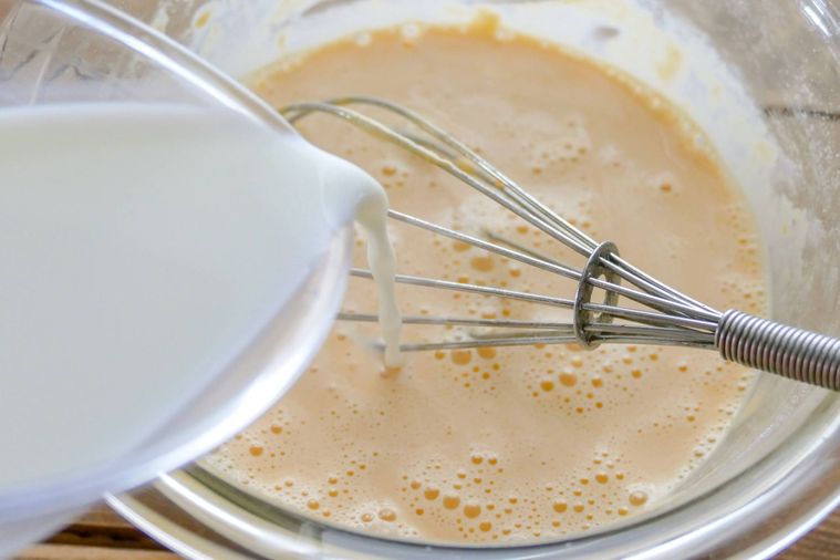 卵液が入っているボウルに牛乳を加える様子