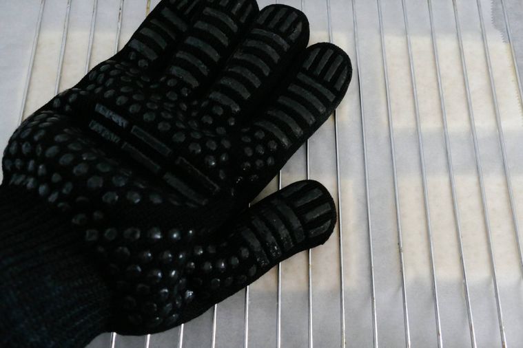 パイ生地にクッキングシートと焼き網を重ね、手袋をした手で押す様子