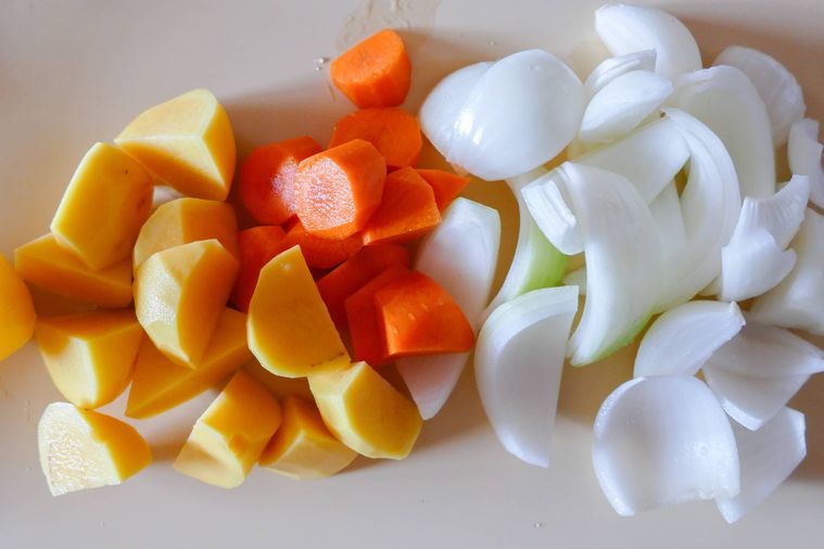 切られたじゃがいも、にんじん、玉ねぎが並ぶまな板