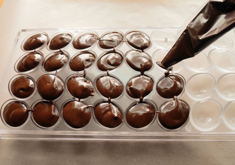 チョコレートの型に、絞り袋に入れたチョコレートを流し入れる様子