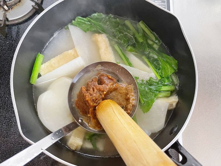 かぶと油揚げ、かぶの葉を煮た鍋に味噌を溶き入れる様子