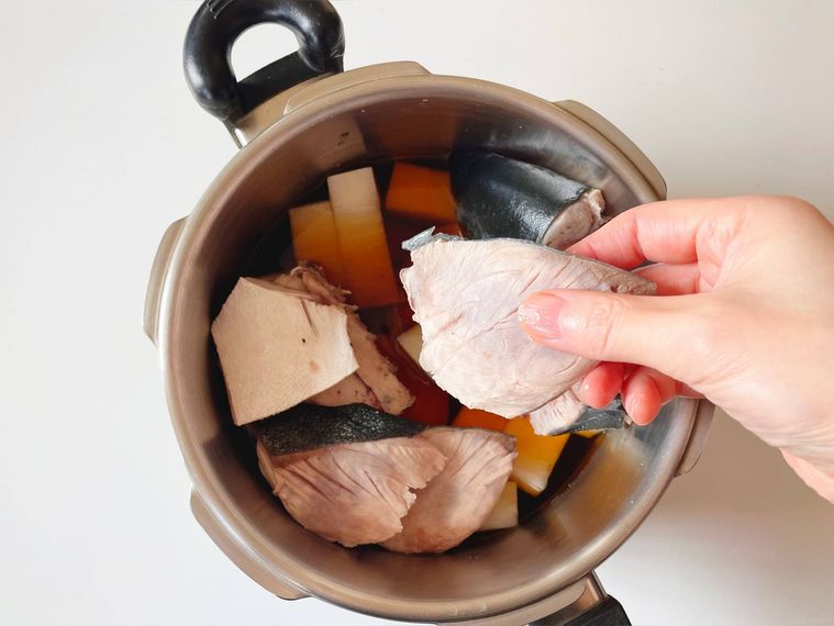 大根と調味料が入った圧力鍋に霜降りのぶりを並べる様子
